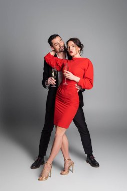Zarif bir kadının erkek arkadaşına sarılıp gri arka planda şampanya tutması. 
