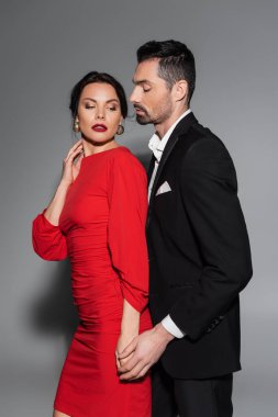 Gri arka planda kırmızı elbiseli seksi kız arkadaşının eline dokunan zarif bir adam. 