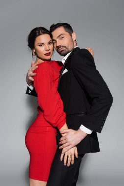 Zarif bir çift, gri arka planda sarılıp kameraya bakıyor. 