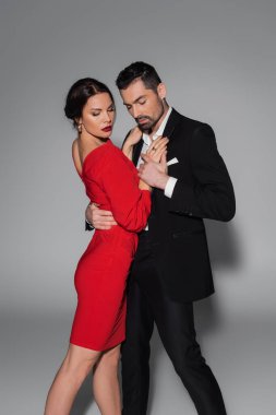 Takım elbiseli esmer adam, gri arka plandaki zarif kız arkadaşına sarılıyor ve ona dokunuyor. 