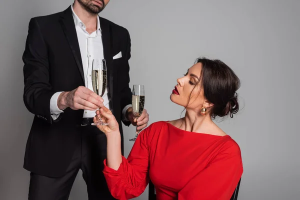 Man in formal wear giving champagne to girlfriend with burgundy lips isolated on grey