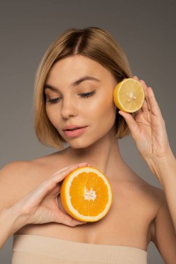 Gri üzerinde sulu portakal ve ekşi limon tutan genç bir kadın. 