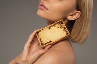 cropped view of blonde young woman holding wooden frame with sweet honey isolated on grey  clipart