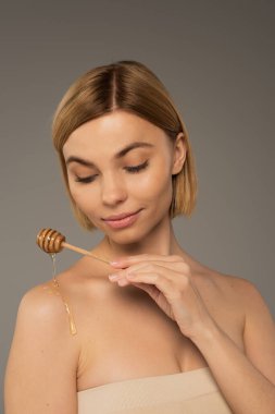 Gri yolda çıplak omzunun yanında tatlı ballı dipper tutan genç bir kadın.