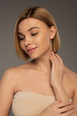 Güzel bir kadın, çıplak omuzlarıyla uzaklara bakıyor ve gri renkte sırıtıyor. 