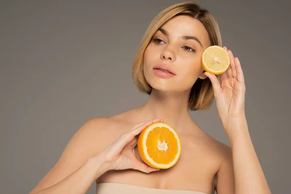 young blonde woman holding juicy orange and sour lemon isolated on grey