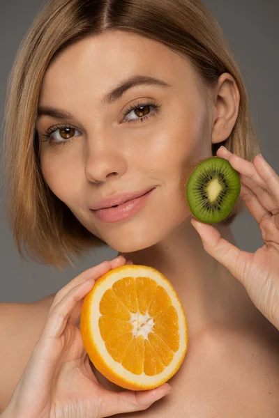 Sulu portakal ve kivi taşıyan neşeli sarışın kadının portresi gri renkte izole edilmiş. 