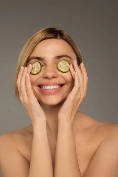 stock image cheerful young woman with naked shoulders and fresh cucumbers on eyes isolated on grey 