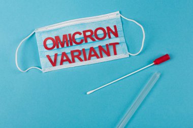 Top view of medical mask with omicron variant lettering near cotton swab on blue background 