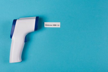 Top view of pyrometer near omicron xbb lettering on blue background 