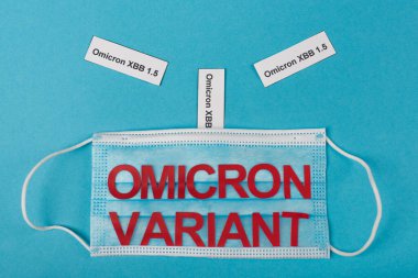 Top view of medical mask and omicron xbb lettering on blue background 