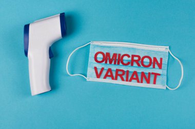 Top view of pyrometer near medical mask with omicron variant lettering on blue background  clipart