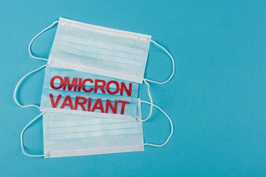 Top view of medical masks with omicron variant lettering on blue background 
