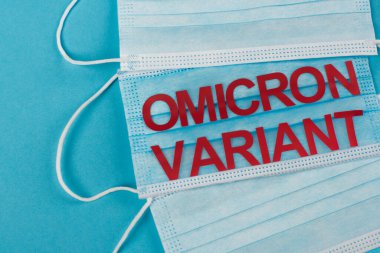 Top view of protective masks with omicron variant lettering on blue background 