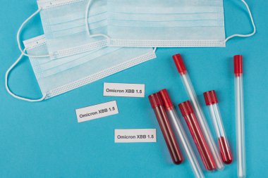 Top view of medical masks near omicron xbb lettering and test tubes on blue background 