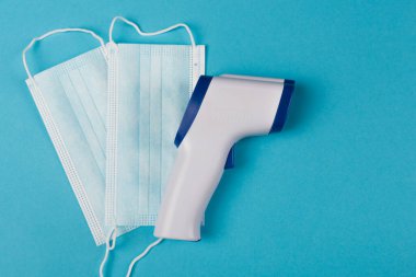 Top view of pyrometer near medical masks on blue background 