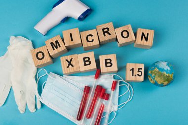 Top view of wooden cubes with omicron xbb lettering near test tubes with blood samples and globe on blue background 