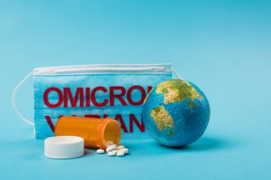 Globe and pills near medical mask with omicron variant lettering on blue background 