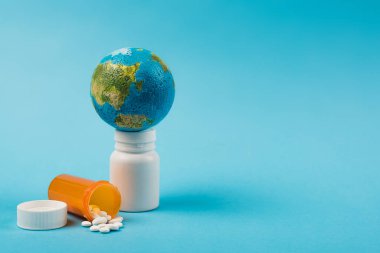 Small globe on globe with pills from new omicron strain on blue background 