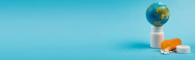 Small globe on jar with pills from new omicron strain on blue background with copy space, banner 