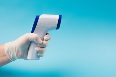 Cropped view of doctor in latex gloves holding pyrometer isolated on blue 