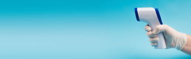 Cropped view of doctor in latex glove holding non-contact pyrometer isolated on blue, banner 