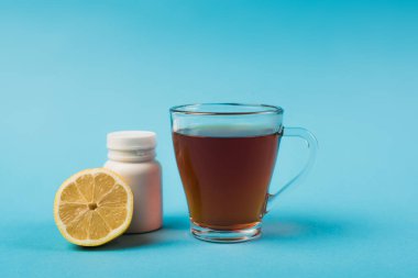 Cup of tea near lemon and pills on blue background 