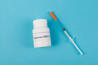 Top view of pills with omicron xbb lettering near syringe on blue background 