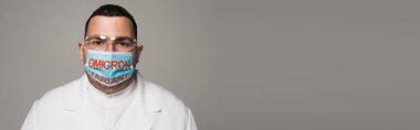 Doctor in protective goggles and medical mask with omicron variant lettering isolated on grey, banner 