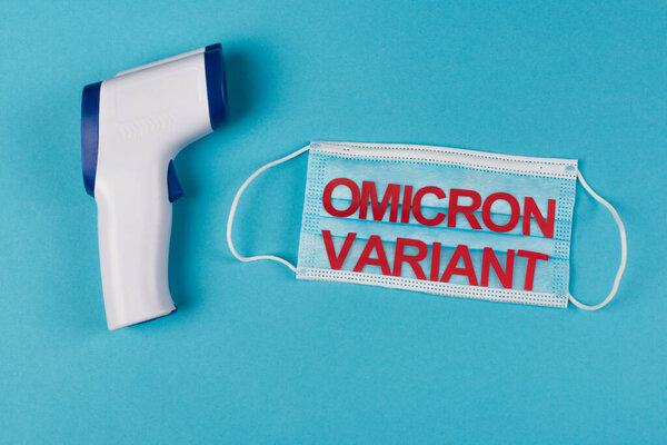 Top view of pyrometer near medical mask with omicron variant lettering on blue background 