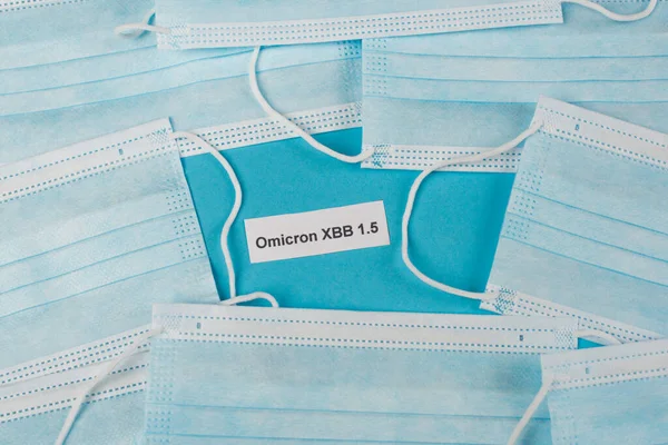 Top view of omicron xbb lettering near medical masks on blue background