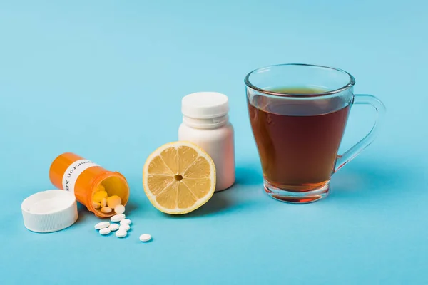Pills with omicron lettering near lemon and cup of tea on blue background