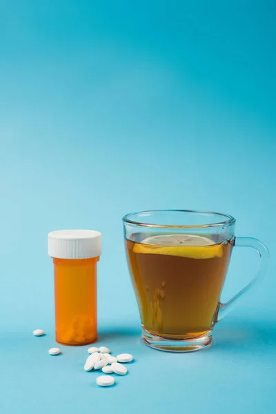 Pills near cup of tea with lemon on blue background