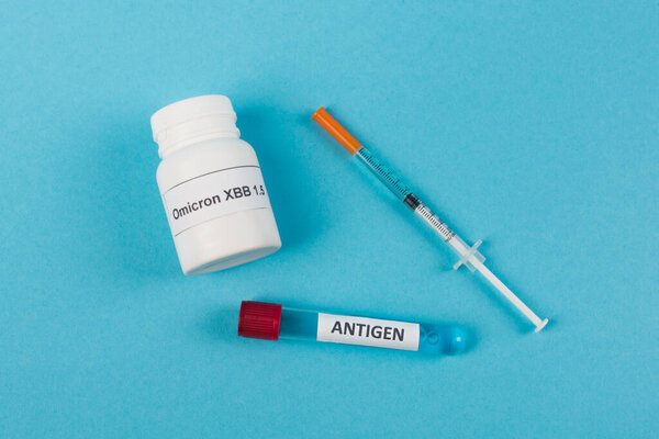 Top view of antigen near pills with omicron xbb lettering and syringe on blue background 