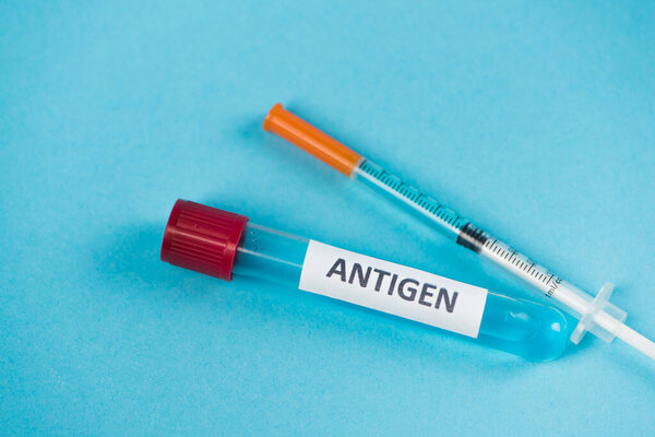 Close up view of syringe and test tube with antigen lettering on blue background 