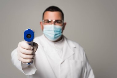 Tıbbi maskeli bulanık doktor, pirometreyi gri renkte tutuyor. 