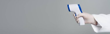 Cropped view of doctor holding non-contact pyrometer isolated on grey, banner 