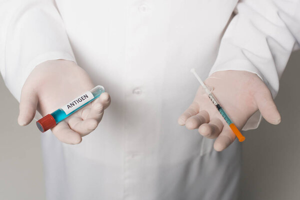 Cropped view of scientist in latex gloves holding syringe and test tube with antigen lettering on grey background 