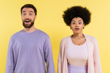 surprised bearded man and curly african american woman standing with open mouth isolated on yellow