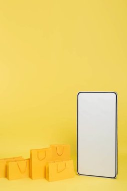 vertical view of shopping bags near huge smartphone template on yellow background