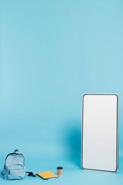 vertical view of white phone template near backpack and notebooks with paper cup on blue background clipart