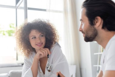 cheerful young woman holding spoon and looking at bearded boyfriend in kitchen 