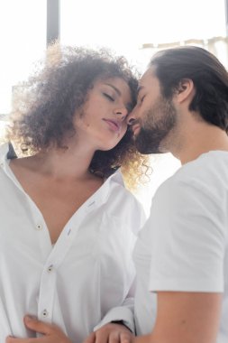 low angle view of bearded man with closed eyes near sensual girlfriend in white shirt 