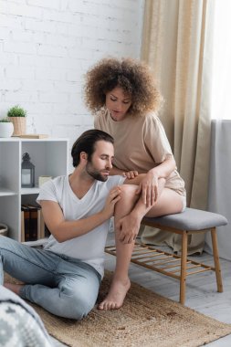curly woman sitting on bed bench near bearded man in white t-shirt 