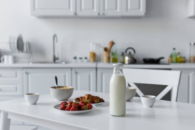 glass bottle with milk near tasty breakfast on table in kitchen  clipart