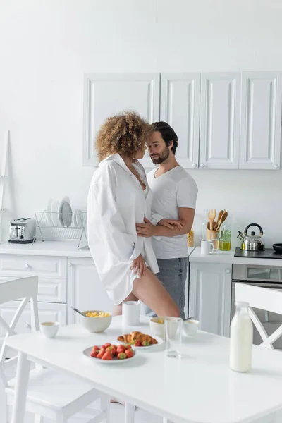 young man in jeans seducing sensual woman in white shirt in kitchen