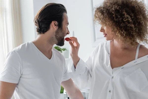 curly woman feeding bearded boyfriend with fresh strawberry