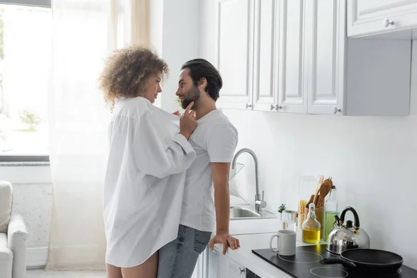 young woman in shirt seducing bearded man in jeans in kitchen