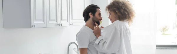 curly and young woman in shirt seducing bearded man in kitchen, banner