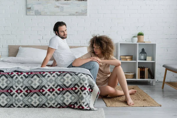 full length of barefoot woman sitting near bearded man in modern bedroom 